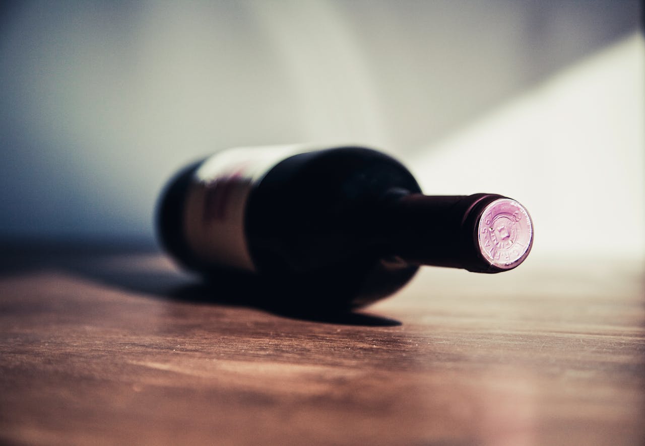 about-03 Close-up of a wine bottle on a wooden table, showcasing elegant shadows and soft lighting.